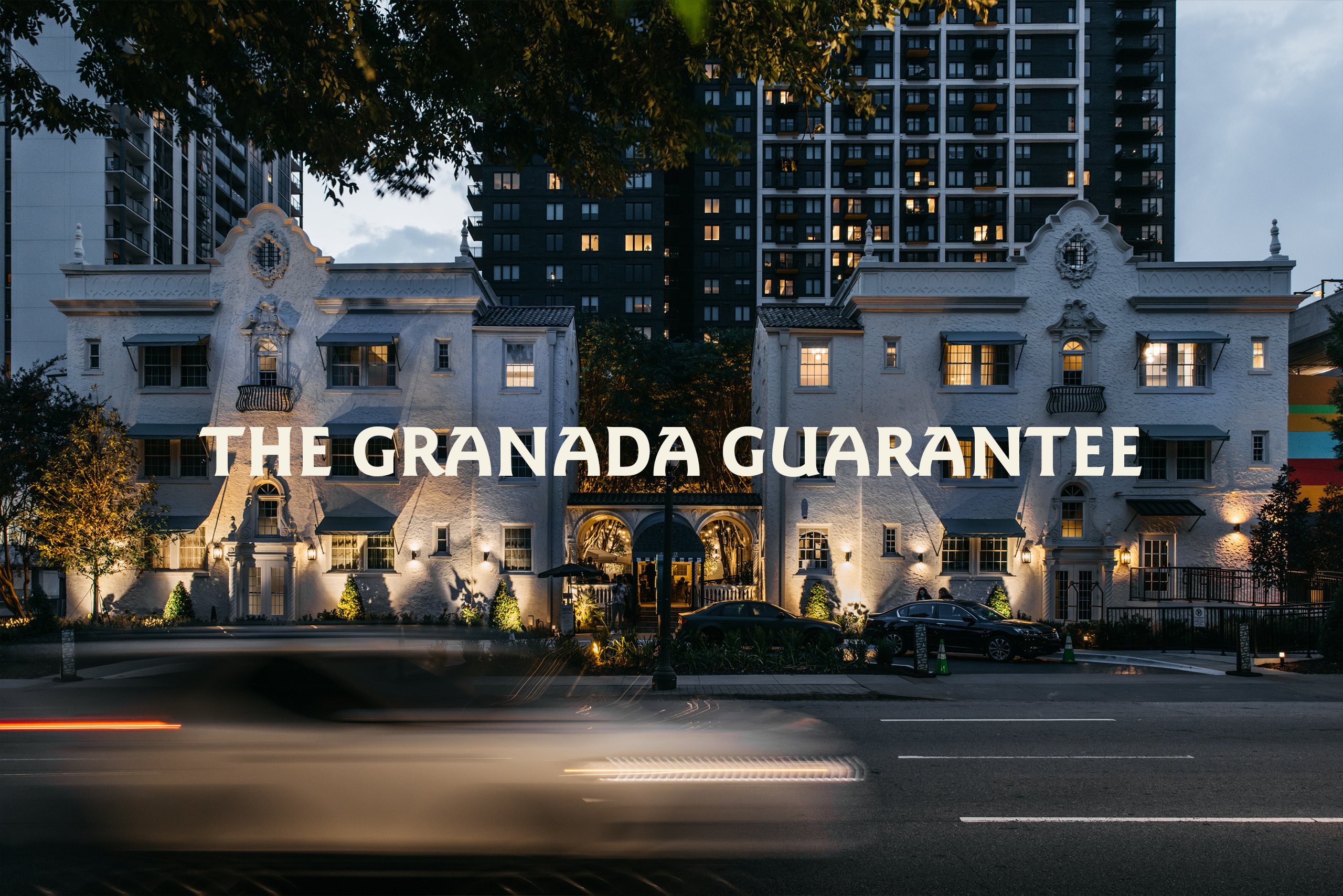 Historic white stucco building with ornate detailing in foreground and a modern high-rise behind; bold text 'THE GRANADA GUARANTEE' across the bottom, dusk lighting.